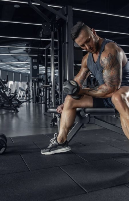 Confident. Young muscular caucasian athlete practicing in gym with the weights. Male model doing strength exercises, training his upper body. Wellness, healthy lifestyle, bodybuilding concept.