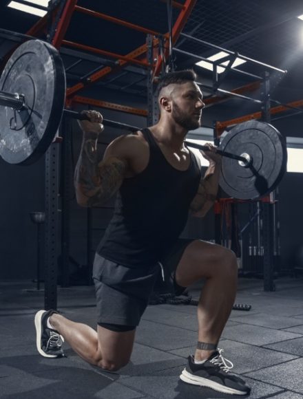 Stronger, Young muscular caucasian athlete practicing lunges in gym with barbell. Male model doing strength exercises, training his lower body. Wellness, healthy lifestyle, bodybuilding concept.
