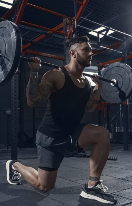 Stronger, Young muscular caucasian athlete practicing lunges in gym with barbell. Male model doing strength exercises, training his lower body. Wellness, healthy lifestyle, bodybuilding concept.